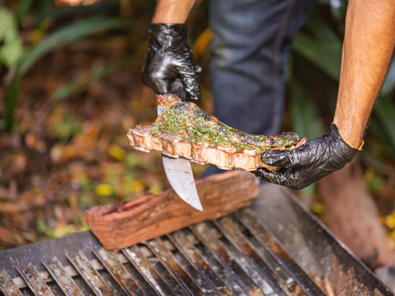 A close up of a person holding a grilled steak at a BBQ cooking class