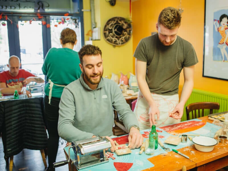 Two men are making colourful handmade pasta in a class.