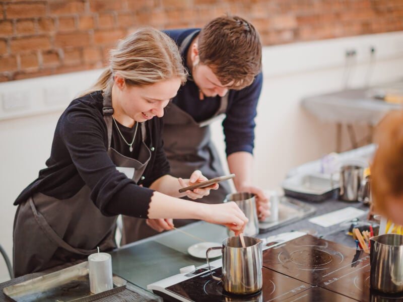 A couple inspect their silver jugs as they melt wax at a candle making workshop.