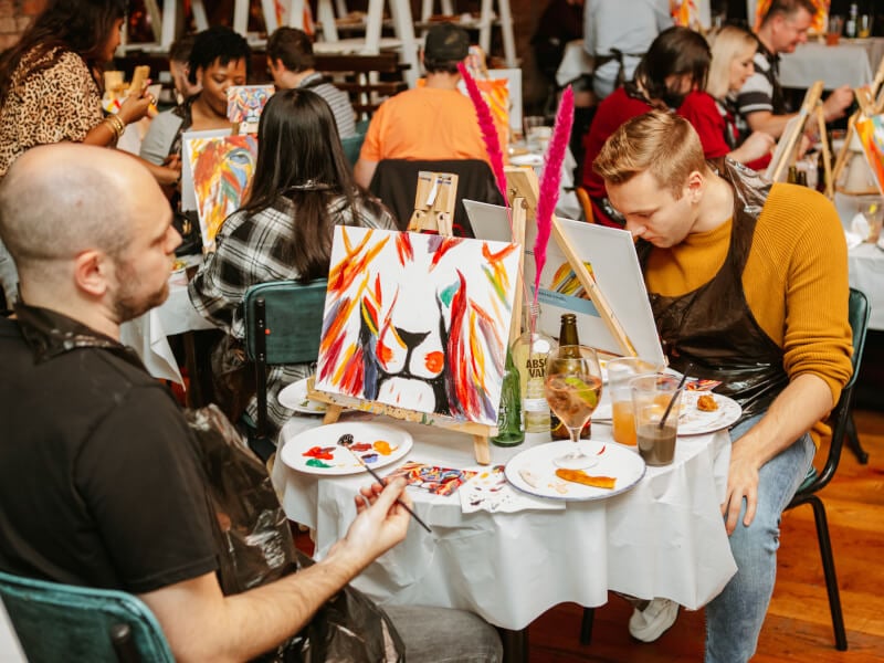 A group of people are learning to paint a colourful lion.