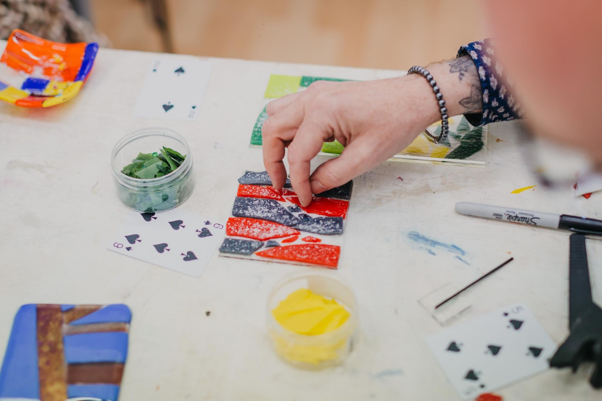 A person makes a fused glass coaster using strips of blue and red glass.