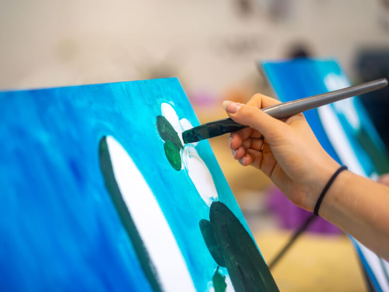 Close-up image of a person painting at an art class.
