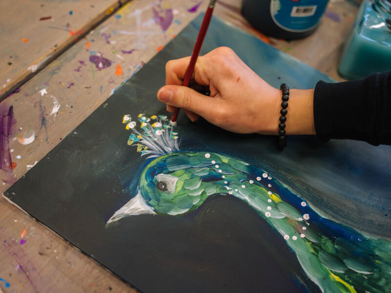 A close up of a person painting a peacock in blue and green paint