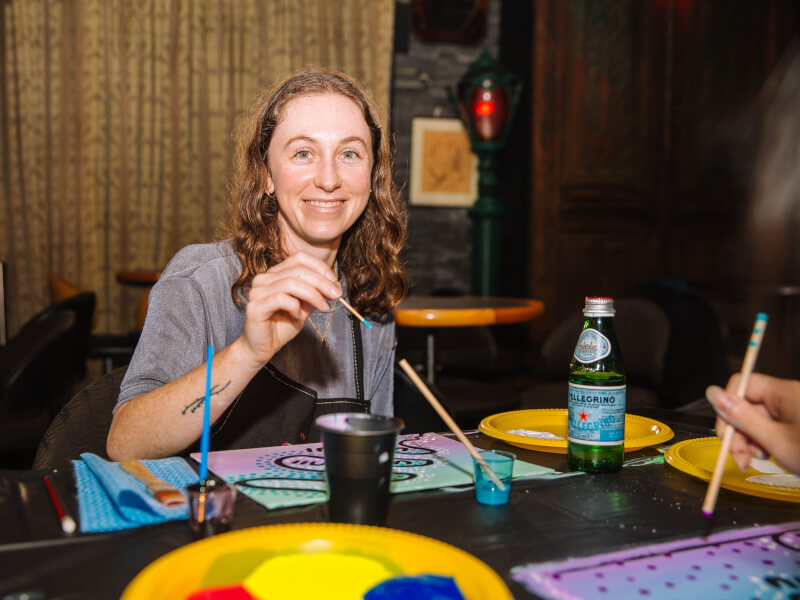 A woman is painting a brightly coloured picture on canvas at a sip and paint class