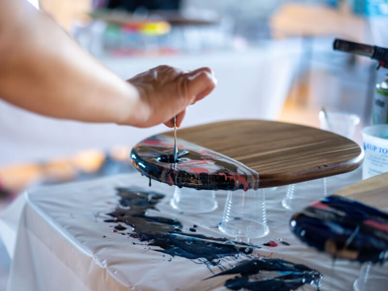 A person is decorating a chopping board with the paint pouring technique