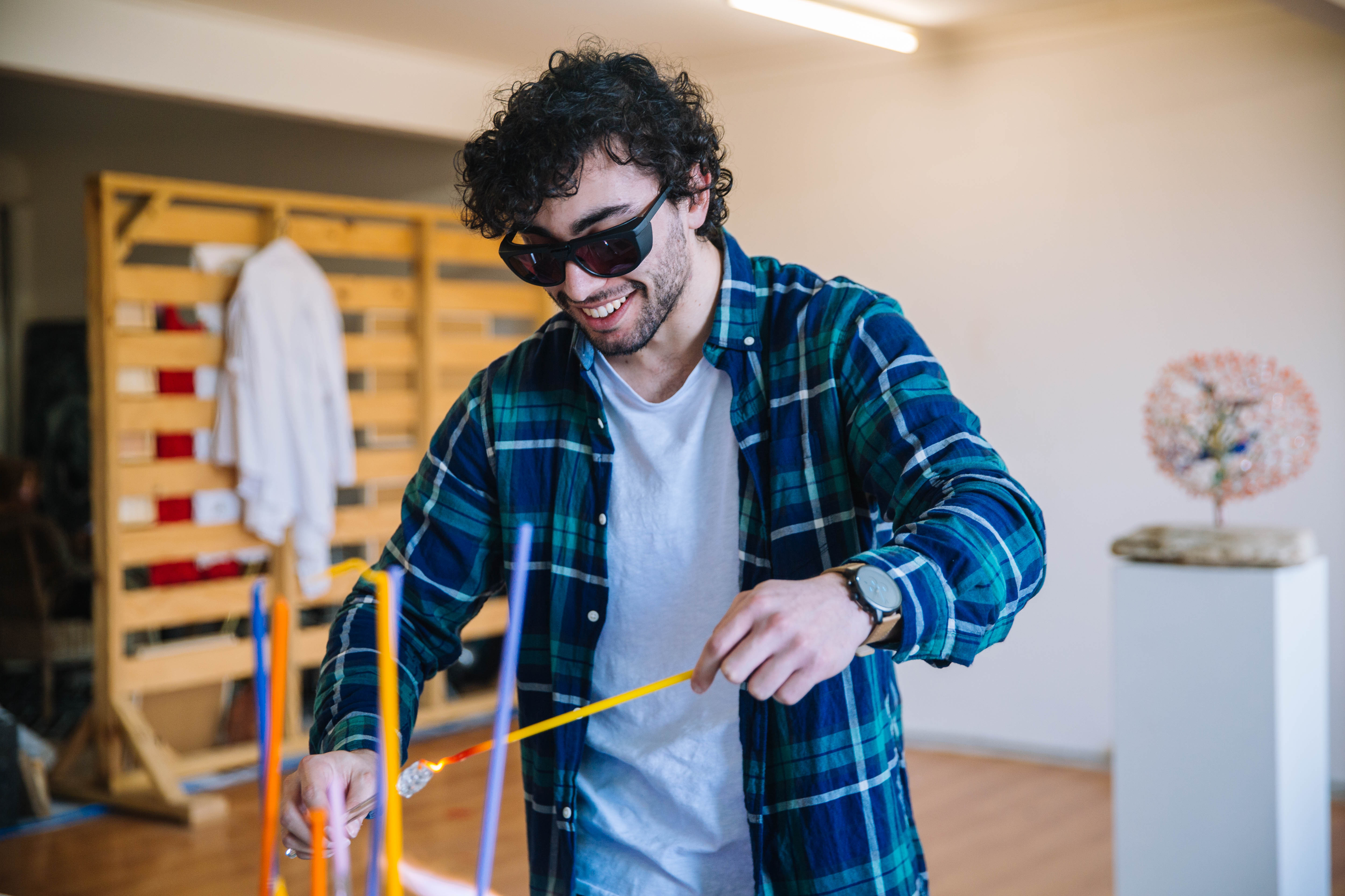 A man is shaping glass on a stick with a red hot poker at a glassblowing class