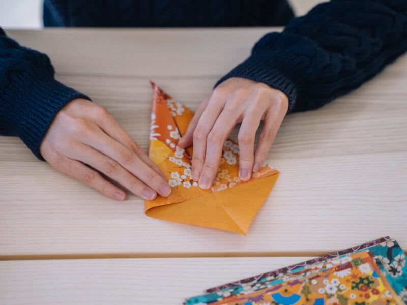 A woman is folding paper to make origami flowers.