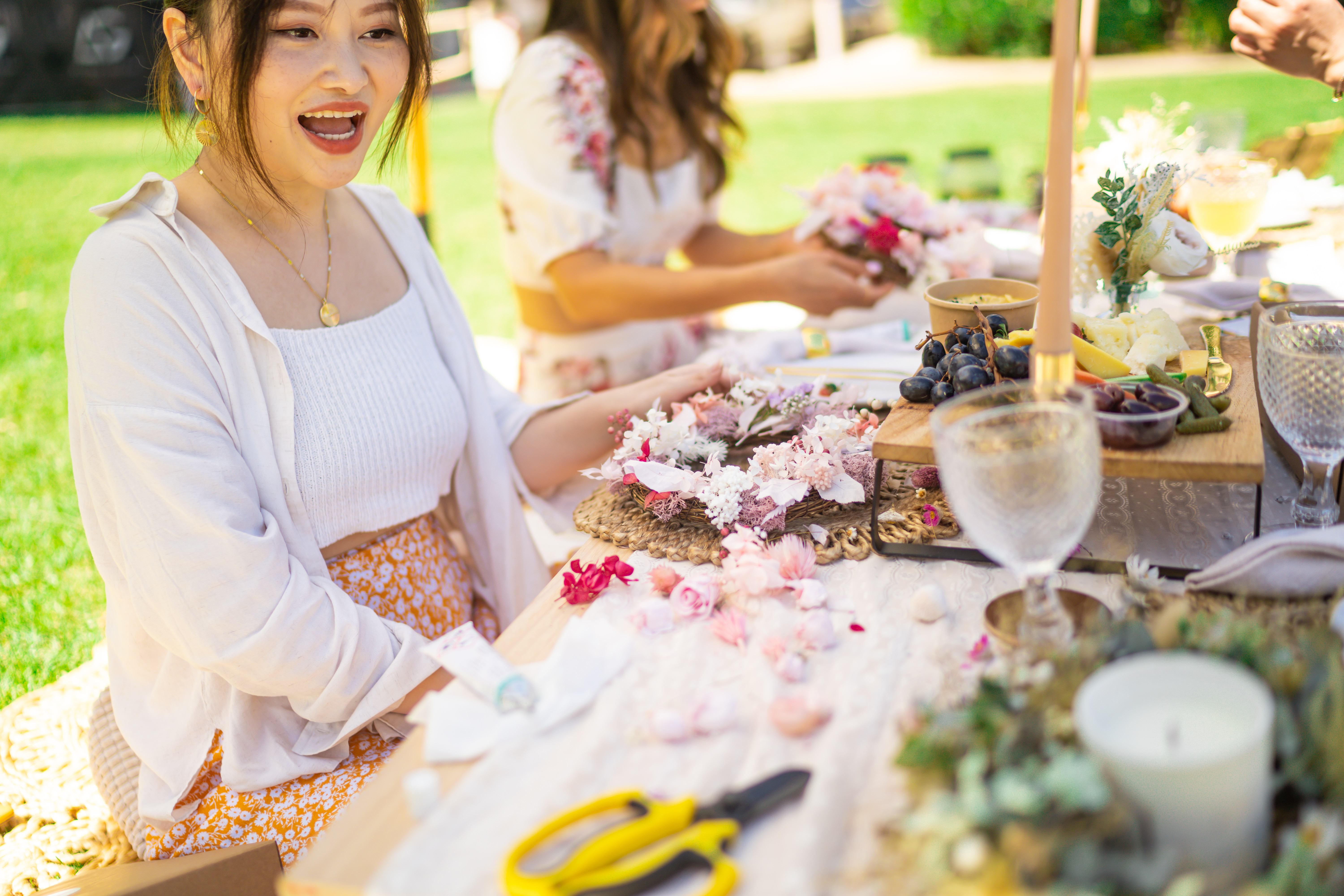 A group of women making flower crowns outdoors on a sunny day
