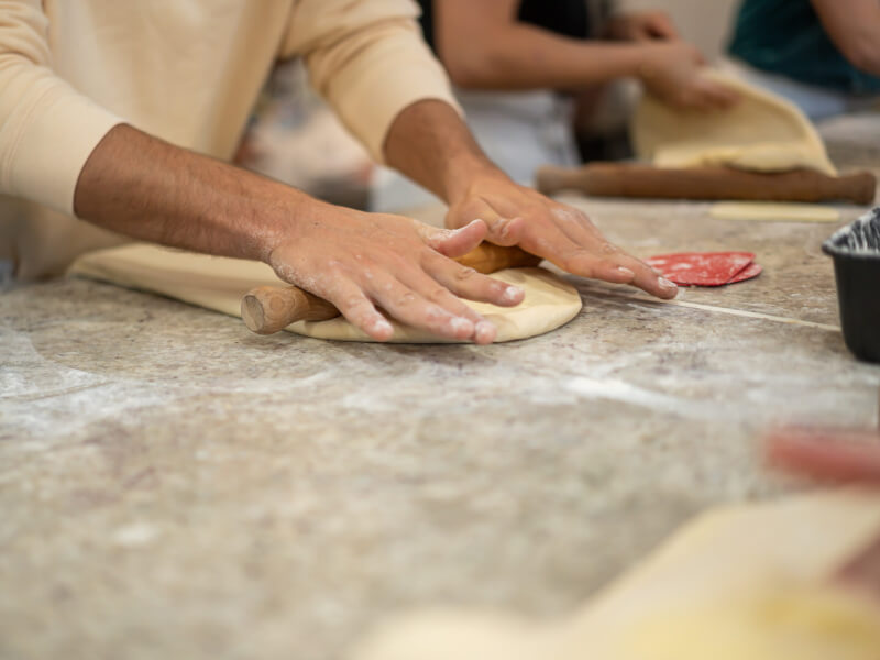 A close up shot of people rolling out dough for handmade pizzas