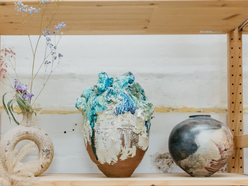 Three handmade clay vases sit on a wooden shelf