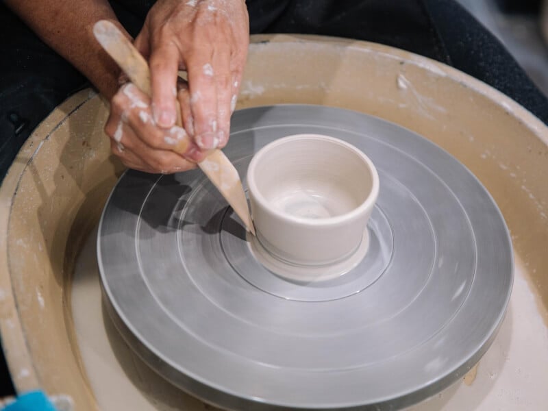 Close up of a person using a wooden tool to shape a pot on a pottery wheel