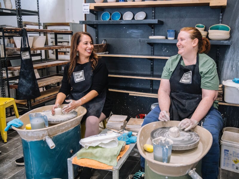 Two women at a potters wheels working on some pottery projects