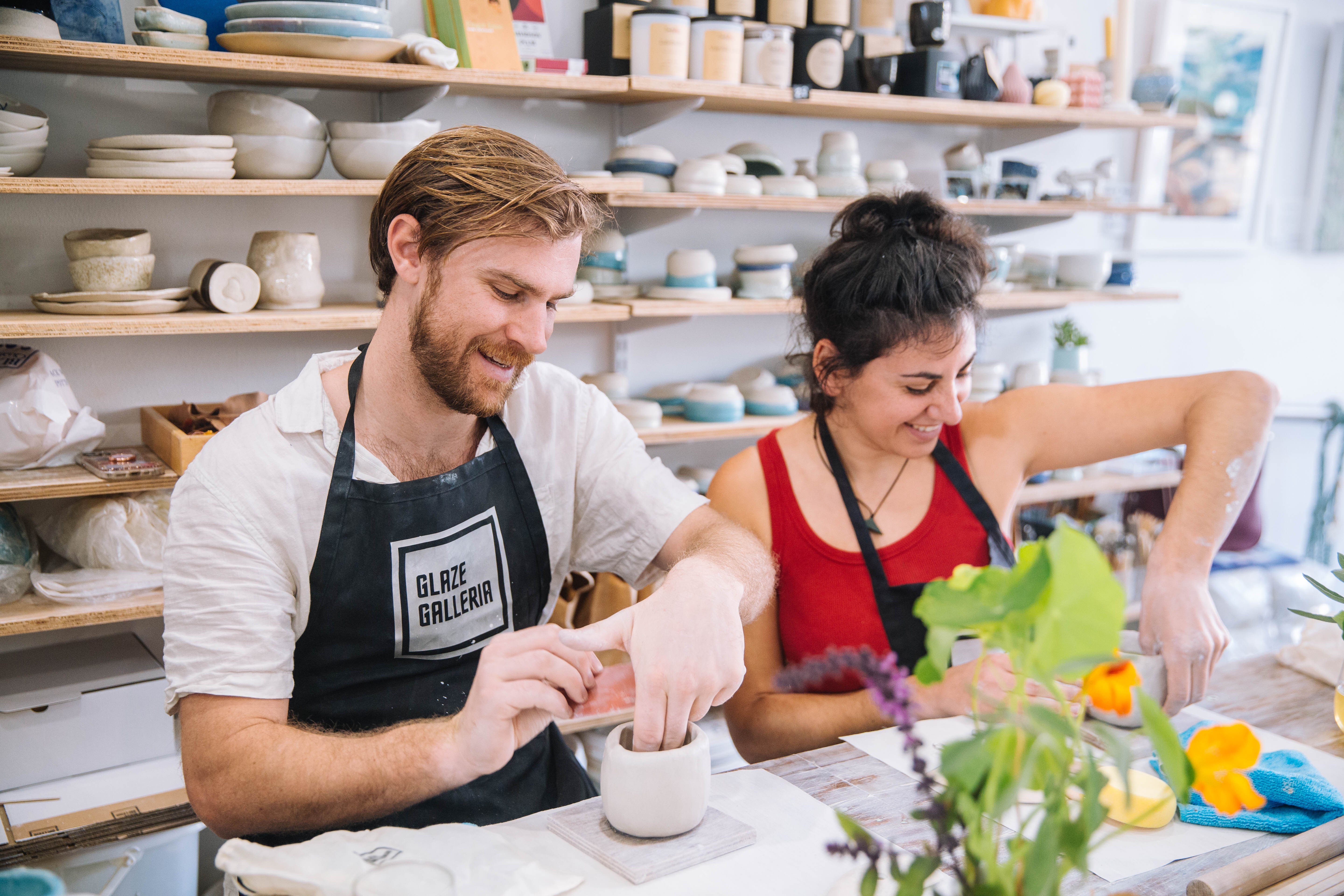 A couple sitting side by side as they work together at a pottery class