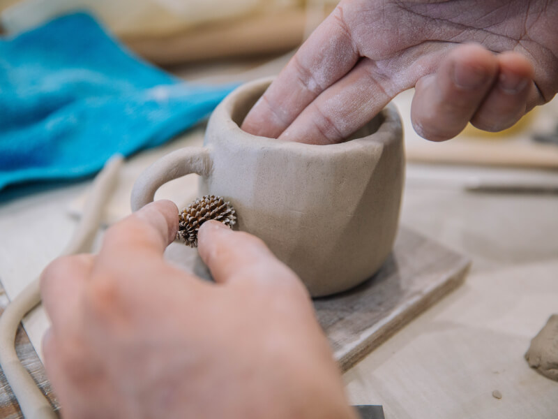 A person is adding a handle to a handmade clay cup
