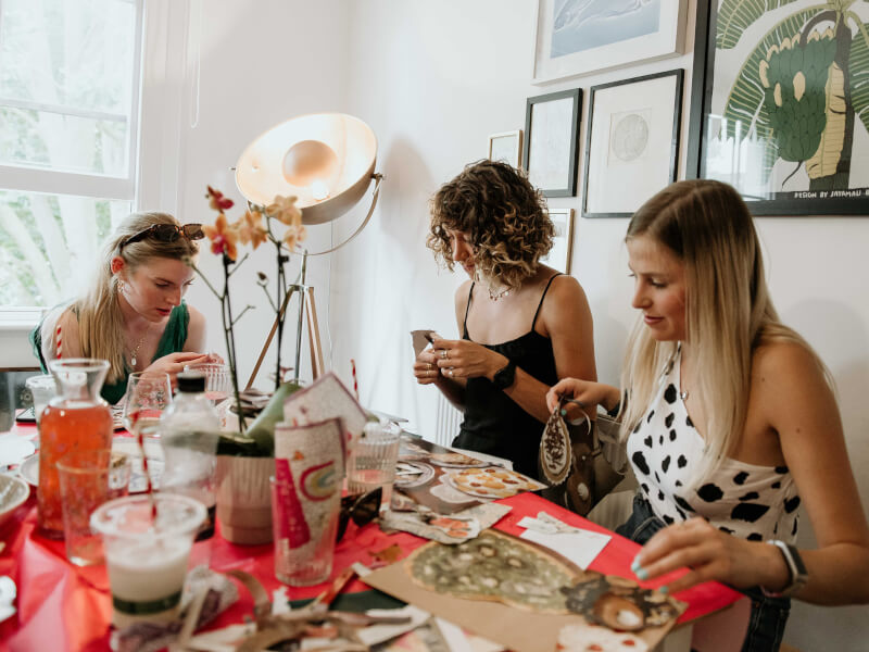 Three women are sitting at a table, making artwork using collage techniques