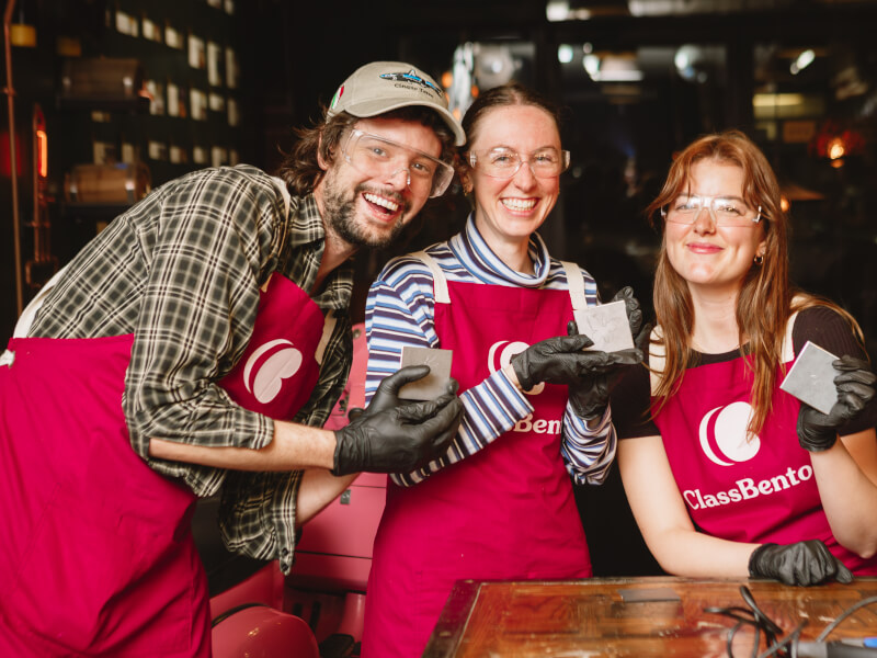 A group of people at a metalwork class, holding up their designs