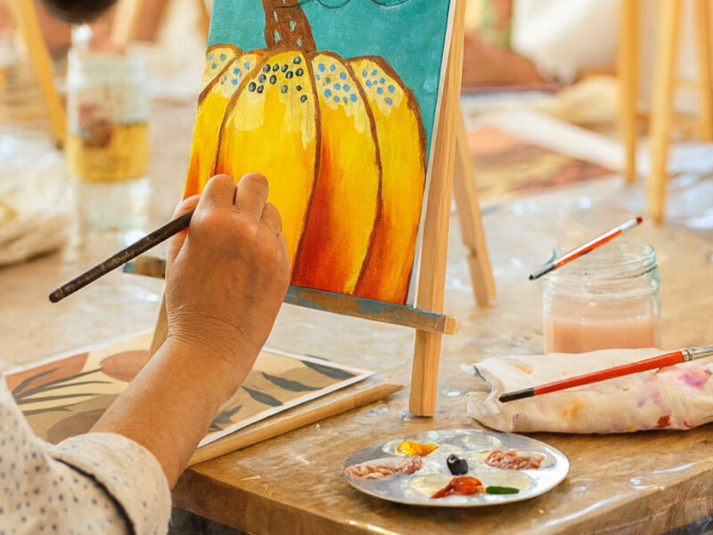 A person is painting a pumpkin at an easel