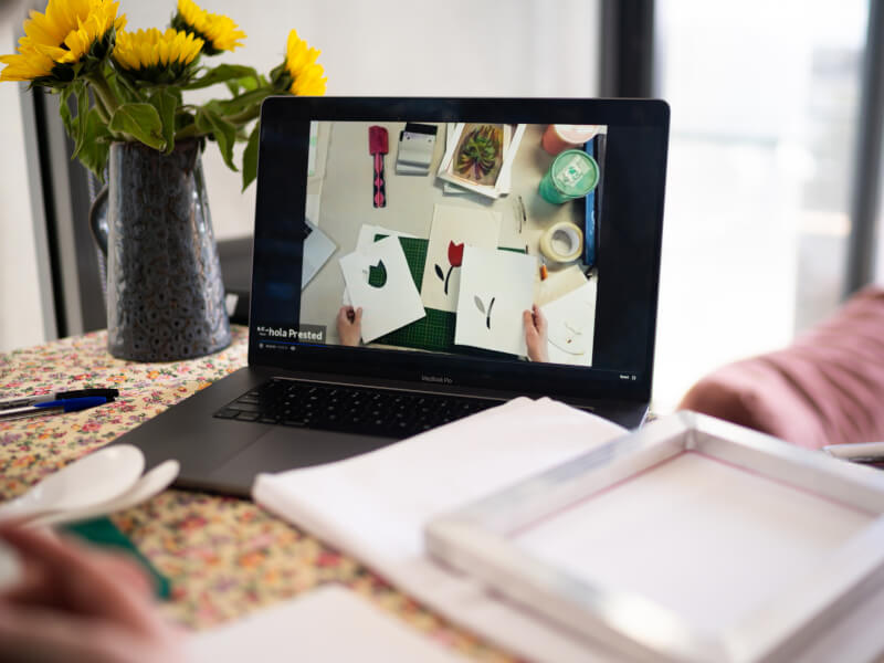 A laptop on a desk with a bunch of yellow sunflowers beside it.