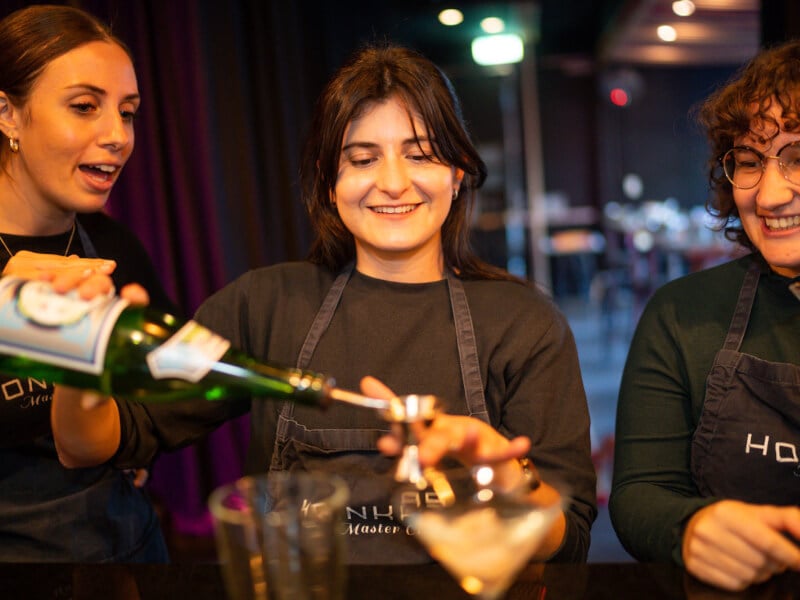 Three women learn to make cocktails together using shot measurements and shakers.
