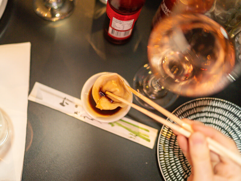 A close up of a person dipping a dumpling into a small bowl of sauce