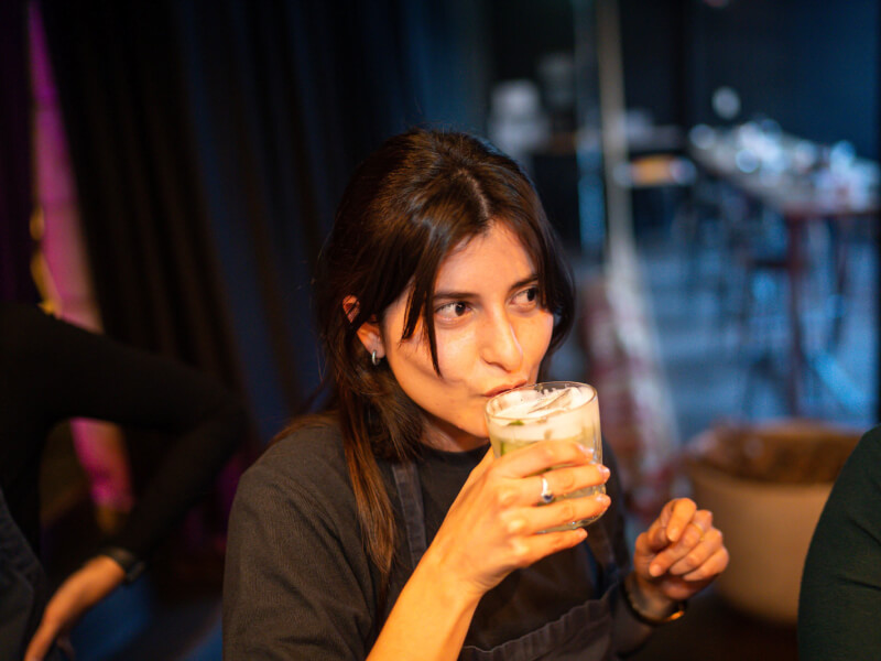 A woman with dark hair sips on their DIY cocktail in a short glass.