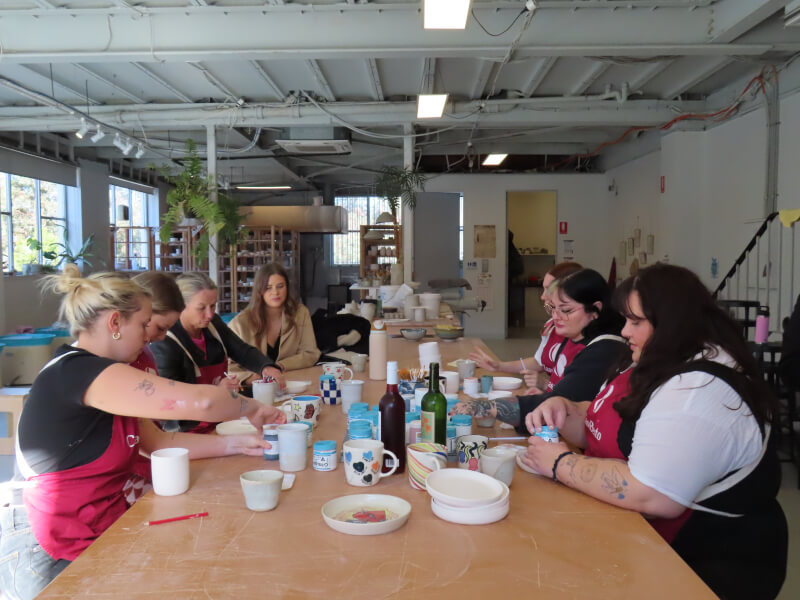 A group of students sitting around a table at a pottery painting class