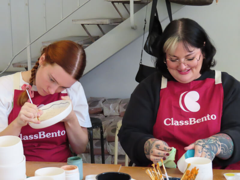 Two women wearing aprons painting pottery