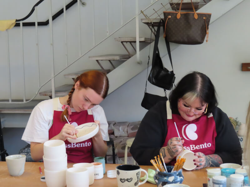Two people sitting side by side at a pottery painting class