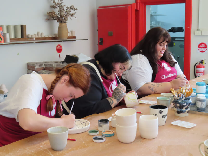 Three students working side by side at a pottery painting workshop