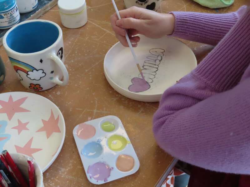 Close up of a person painting a ceramic bowl with lilac paint