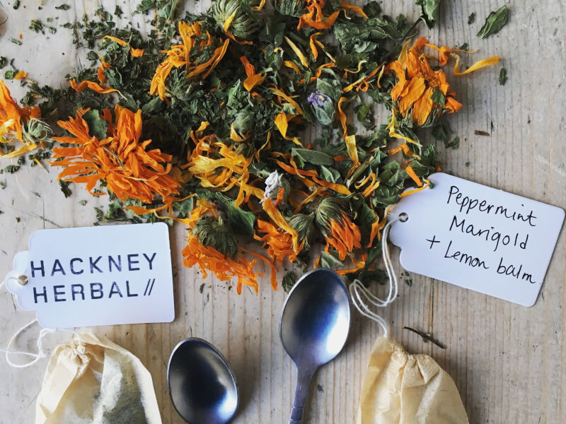 A selection of dried orange flowers sit on a table with handmade teabags