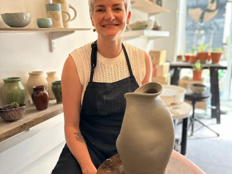 A woman sits in front of a large pot used in a hug pottery class