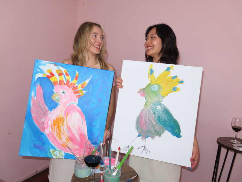 Two students showing off their finished paintings at a sip and paint