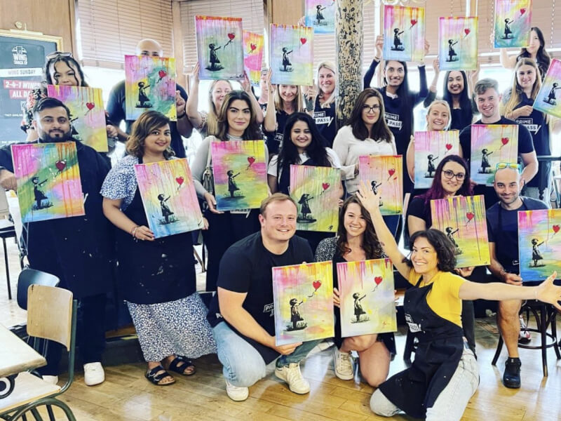 A group of people at a painting class, holding up their finished paintings