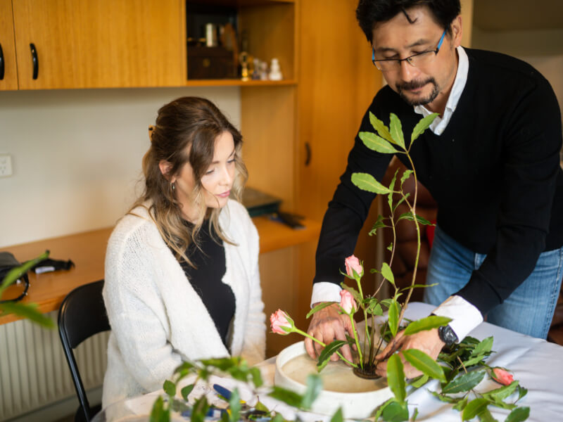 A teacher guides a student in an Ikebana class.