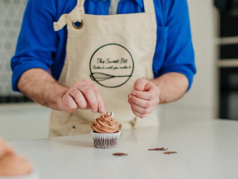 A man decorating a chocolate cupcake