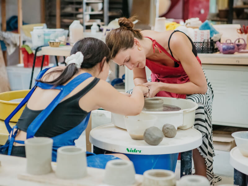 A teacher helping a student at a pottery wheel throwing class