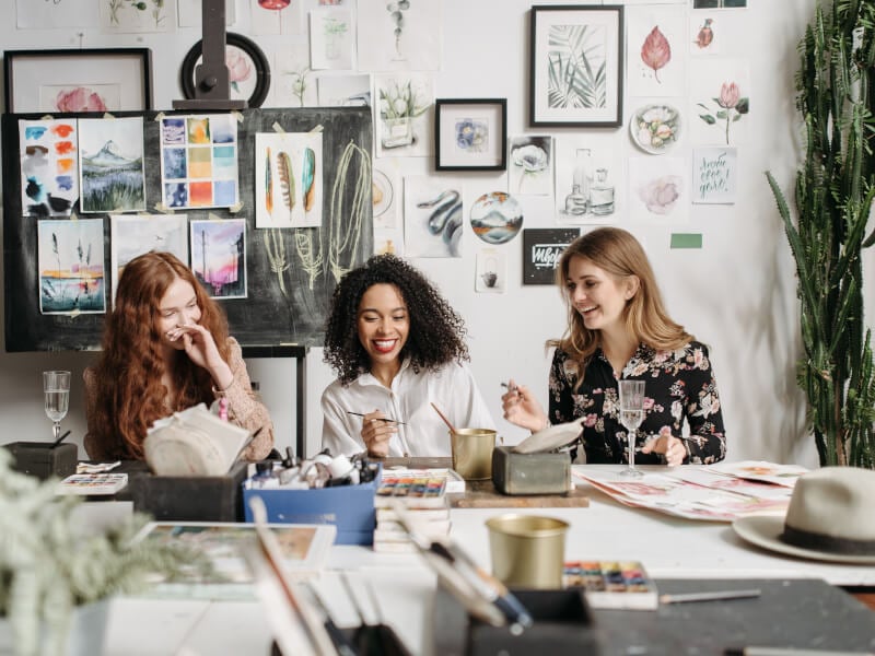 Three women laughing and painting in an art studio