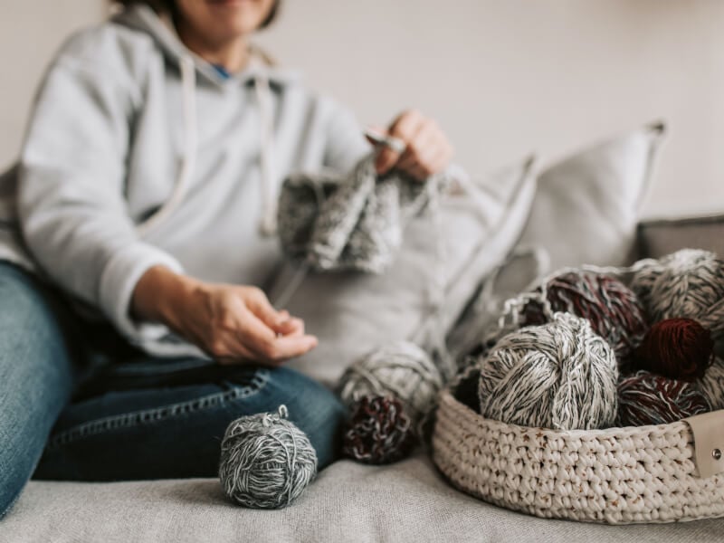 a person sits on a sofa knitting with balls of yarn next to them