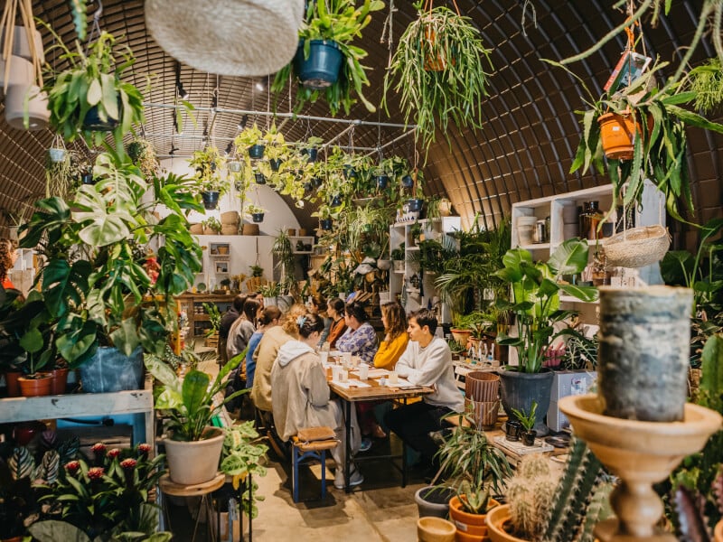A beautiful foliage filled candle making studio with a long bench of makers ready to create candles
