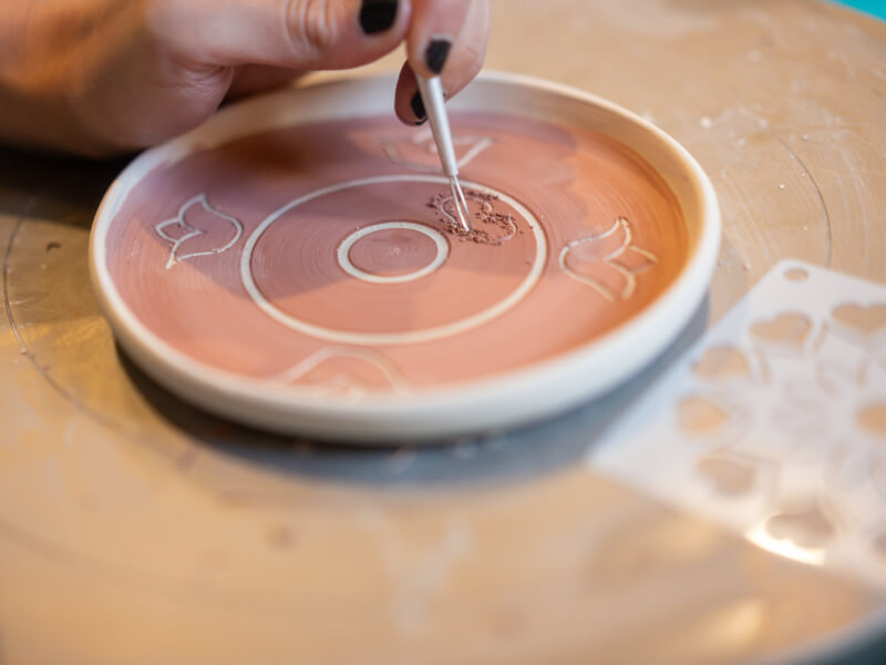 A hand holding a pottery tool whilst carving