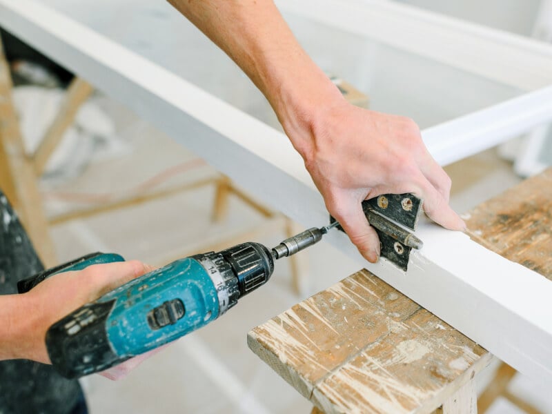 A person is adding hinges to a frame with an electric screwdriver