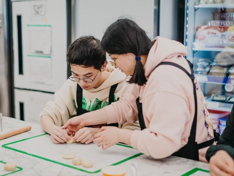 A woman helps a man with glasses to make Chinese buns