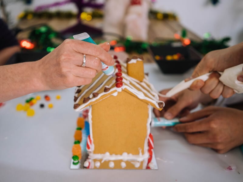Hands icing a DIY gingerbread house