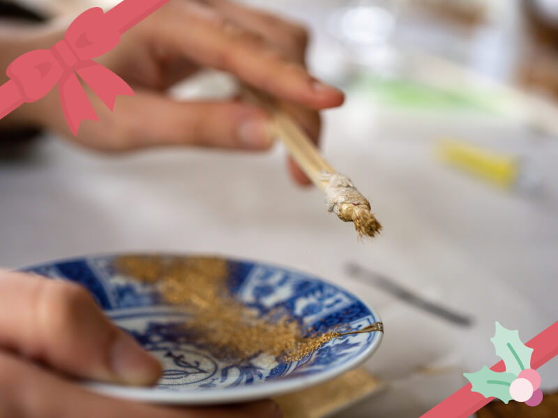 A small blue china plate with gold dust on it and a person's hand holding a brush