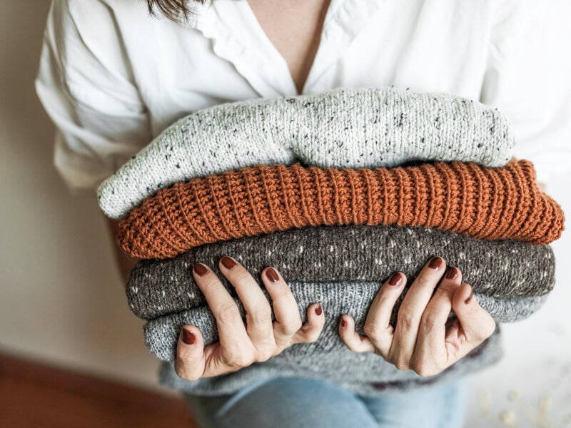 a woman holding a pile of handknitted jumpers