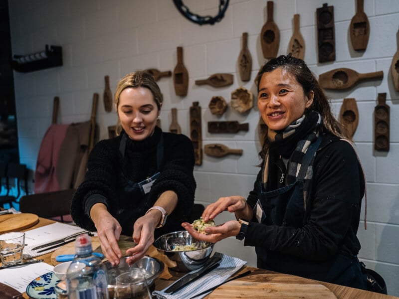 Two women wearing aprons smiling at a cooking class