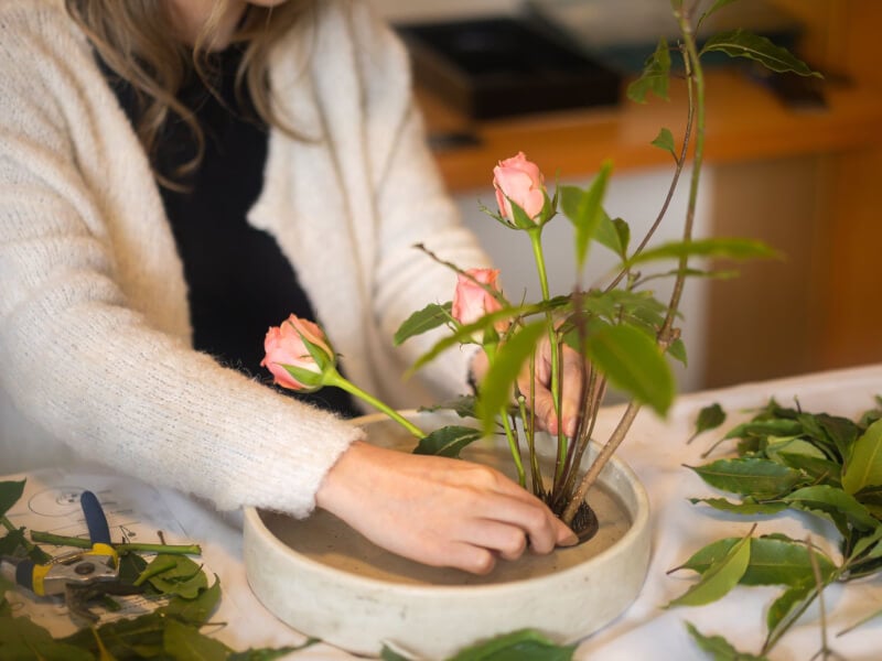 A woman tries makes a floral arrangement with pink flowers