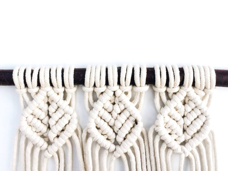 A close up view of a white cotton macrame wall hanging on a dark brown_black hanger
