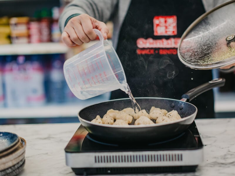 A man pouring water into a pan with dumplings